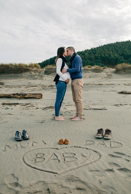 Фото Мама, папа и ребенок написаны на песке, а родители целуются сзади