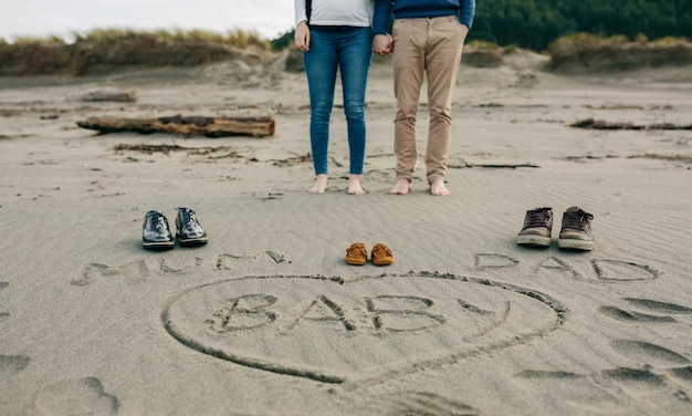 Foto mamma papà e bambino scritti sulla sabbia con dietro i genitori