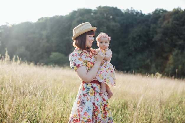 Mum, little daughter outdoors. Happy Mothers Day. Young mother with little cute kid daughter having fun in the field on sunset. Portrait of likable mom with baby together on nature on summer day.