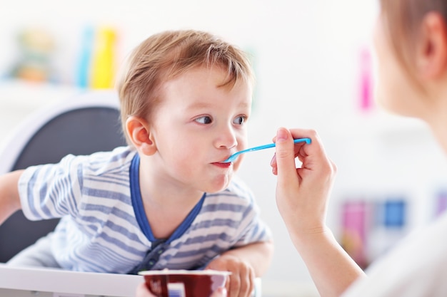 お母さんは子供にスプーンで餌をやる