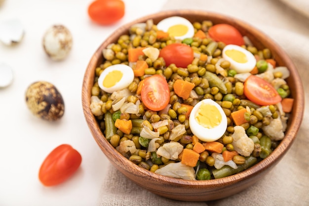 Mung bean porridge with quail eggs, tomatoes and microgreen sprouts on a white wooden background and linen textile. Side view, close up, selective focus.