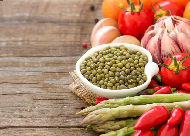 Mung beans in a bowl and vegetables on wood close up