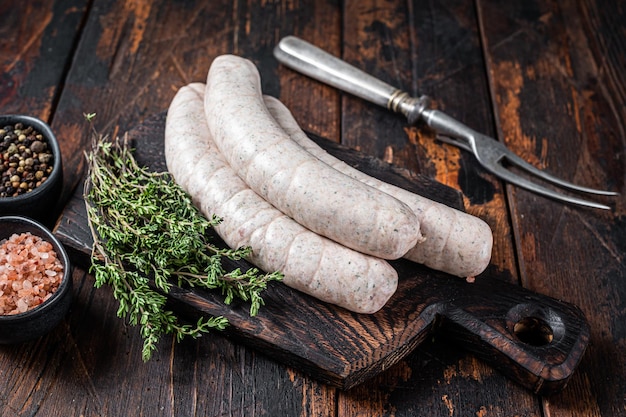 Munich traditional white sausages on a wooden board with thyme. Dark wooden background. Top view.