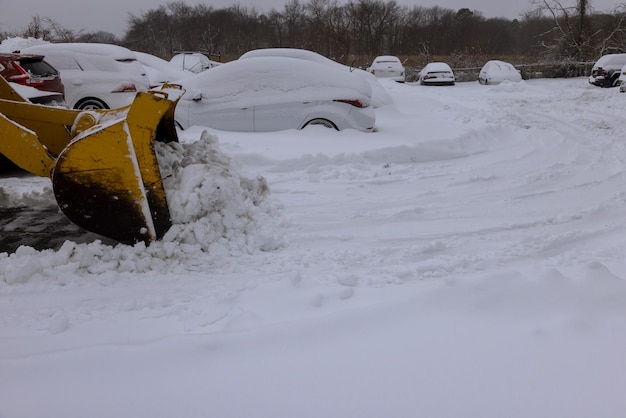 Municipal service tractor removing snow on parking lot for car after snowfall