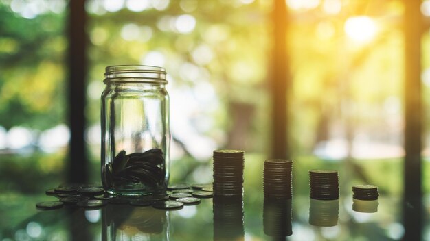 Muntenstapel en een glazen geldpot op tafel voor besparing en financieel concept