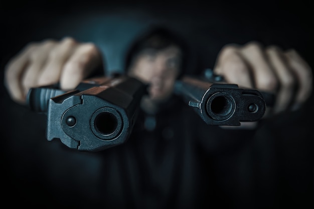 黒い背景の殺人者男の手にある2つのピストルは、2つの銃の銃口のカメラのクローズアップに向けられています...