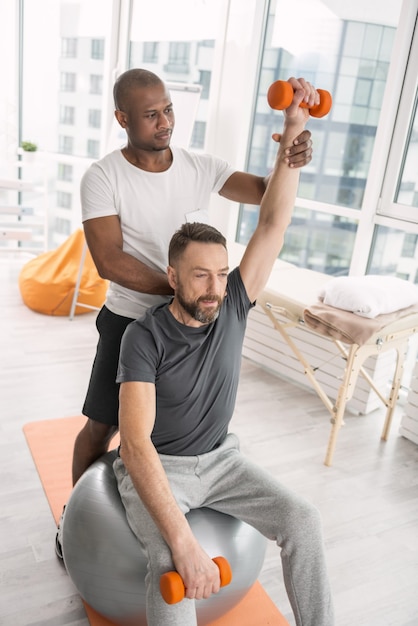 Muscle development. Nice bearded man lifting dumbbells while developing his muscles