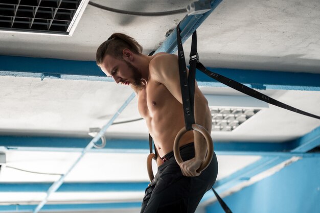 Muscle-up exercise athletic man doing intense workout at gym on gymnastic rings