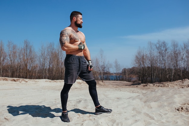 Muscled boxer works out on the sand with a naked torso