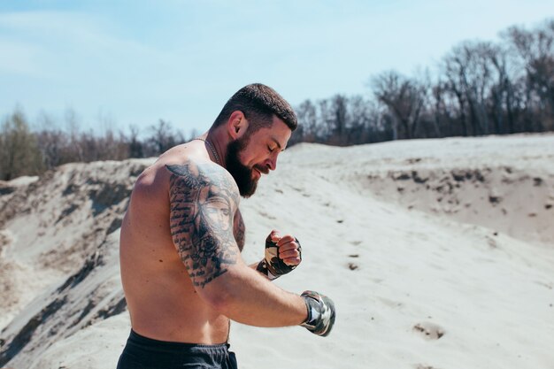 Muscled boxer works out on the sand with a naked torso