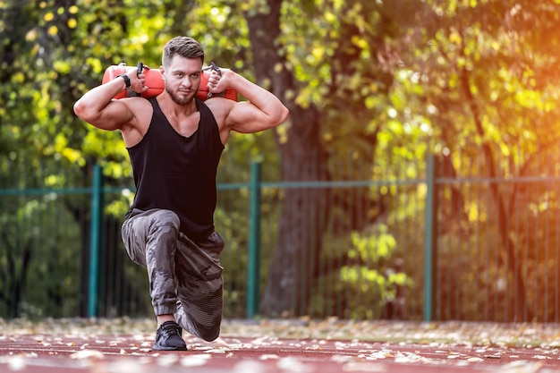 Мускулистый взрослый мужчина делает упражнения с оборудованием Спортсмен тренируется на широком стадионе в зеленом парке
