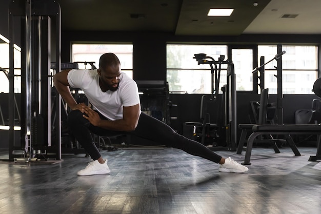 Мускулистый африканец в спортзале делает упражнения на растяжку на полу