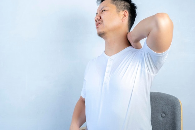 사진 근육이 많은 아시아 남성이 허리와 목 통증을 고 앉아있는 자세가 잘못되어 테이블에 앉아 있습니다.