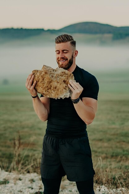 Muscular athlete man trains and exercises with big stone