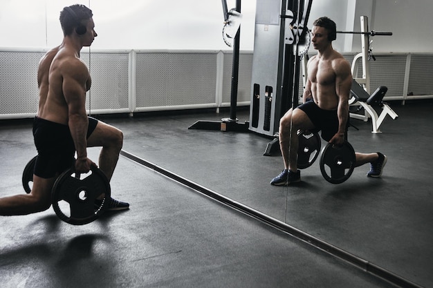 Мускулистый спортсмен с голым туловищем в наушниках на тренировке в тренажерном зале качает свое тело и слушает музыку