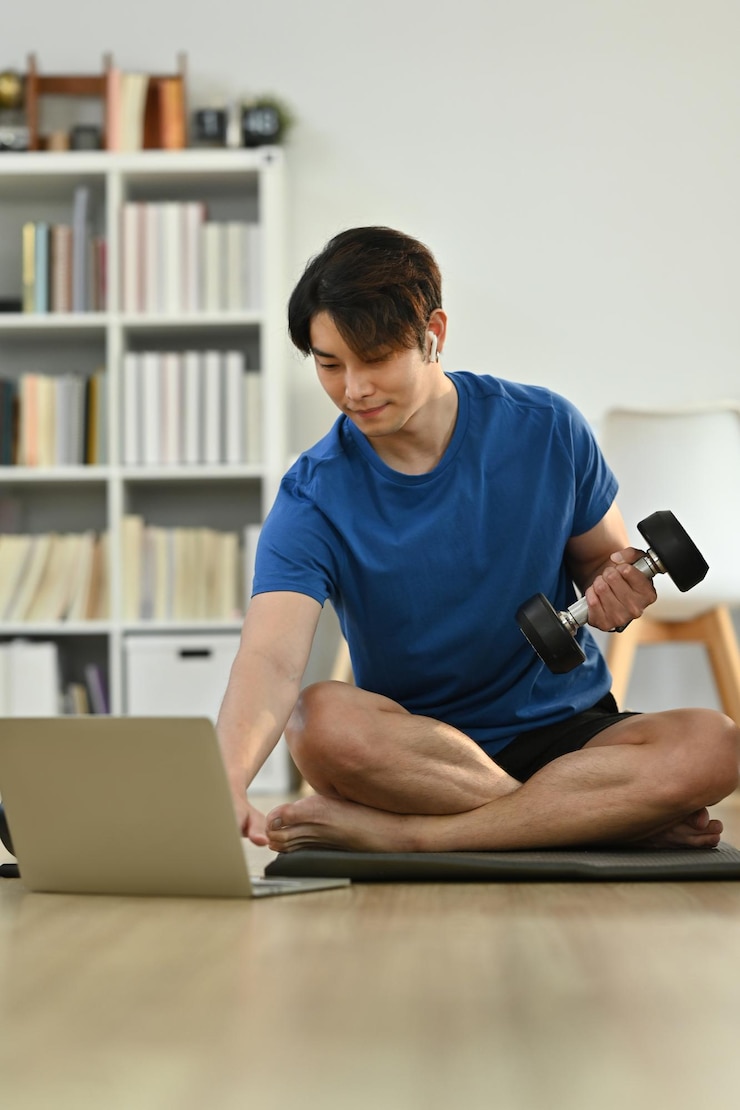Photo 집에서 아침 운동을 하는 동안 아령으로 운동하고 노트북에서 비디오 온라인 교육을 보는 근육질 운동선수