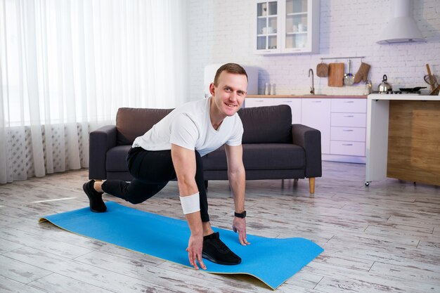 Muscular athletic man in a t-shirt doing warm-up exercises at home. Doing sports at home during the quarantine period. Fitness outside the gym