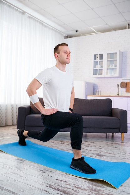 Muscular athletic man in a t-shirt doing warm-up exercises at home. Doing sports at home during the quarantine period. Fitness outside the gym