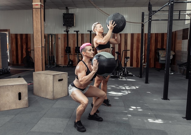 Muscular athletic women train with medicine balls in a modern gym. Cross fit, functional training