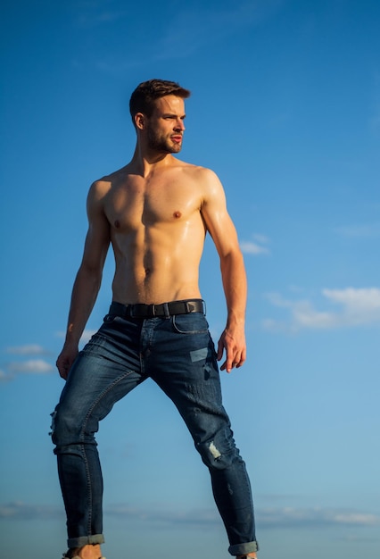 Muscular bare torso Six packs muscular chest Man outdoors blue sky background Summer trends Male beauty concept Hot day Athletic handsome macho wear denim pants Muscular body Fitness model