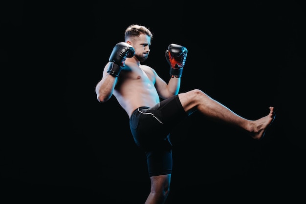 Foto muscoloso pugile faticoso a piedi nudi in guantoni da boxe e pantaloncini facendo calcio isolato sul nero