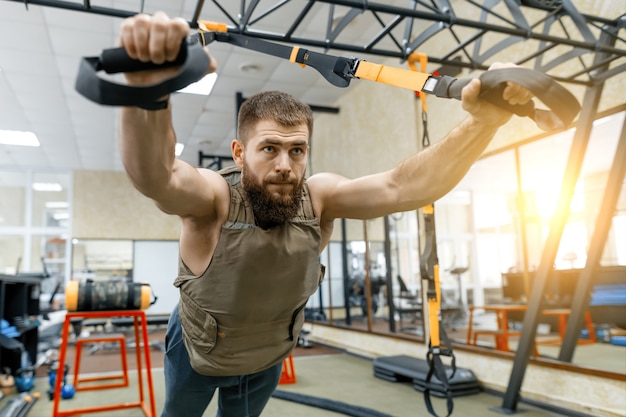 Muscular bearded man dressed in military weighted armored vest doing exercises