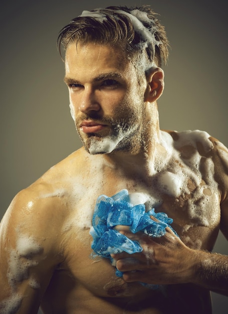 シャワーを浴びている筋肉のひげを生やした男セクシーな男はスポンジスキンケアスパ美容男で体を洗っています