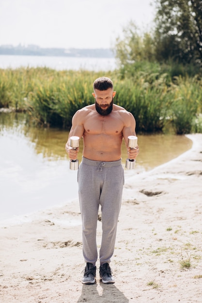 Muscular and bearded mustachioed man doing exercises with dumbbells outdoors. Bodybuilding and outdoor sports concept