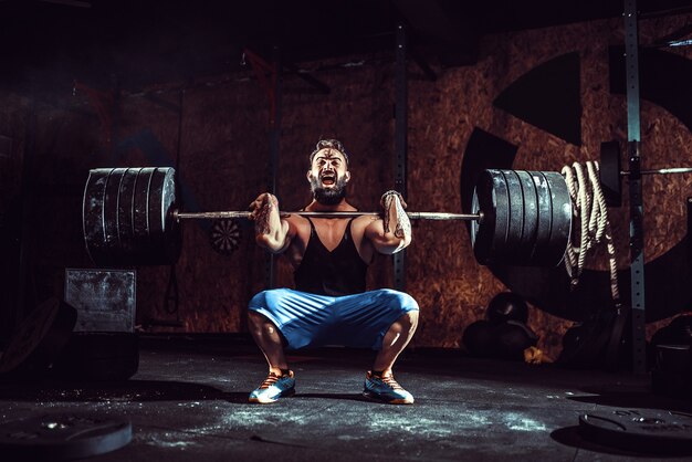 Muscular bearded tattooed fitness man doing deadlift a barbell over his head in modern fitness center. 