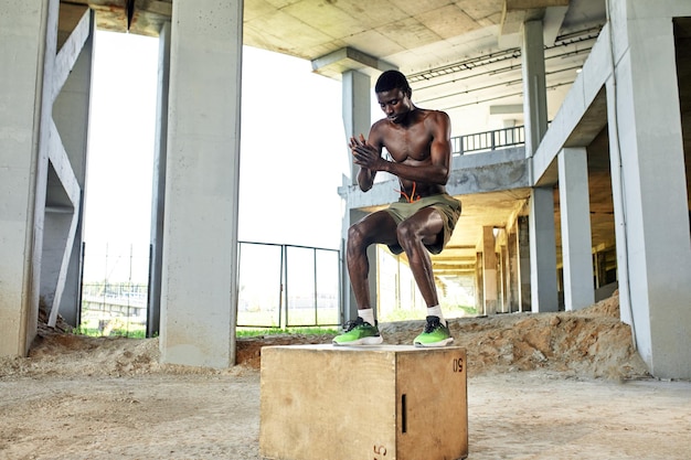 Muscular black athlete jumping on wooden box Urban background