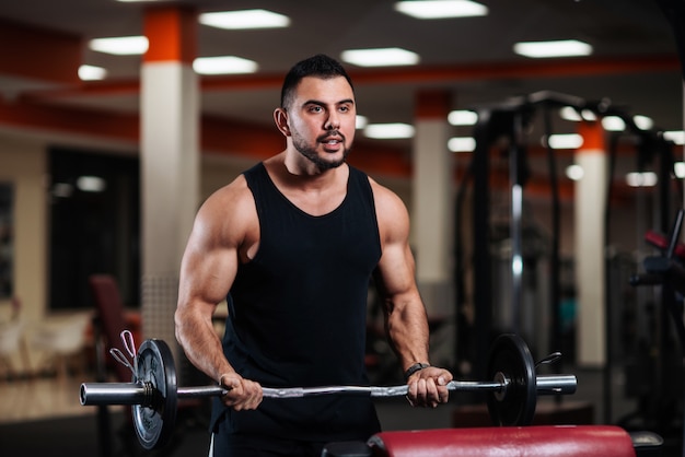  Muscular bodybuilder guy doing exercises with a barbell.