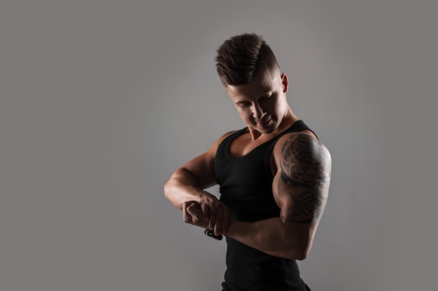 Muscular bodybuilder handsome sports guy model with hair in a black Tshirt showing off his biceps muscles against a dark background