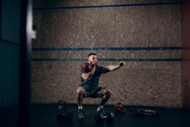 Muscular caucasian bearded man lifting kettlebells in gym.