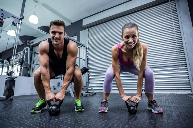 A muscular couple lifting kettlebells