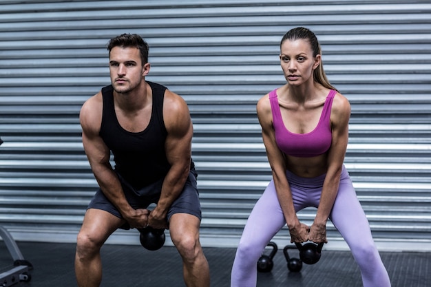 A muscular couple lifting kettlebells