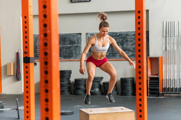 Muscular female athlete jumping on box