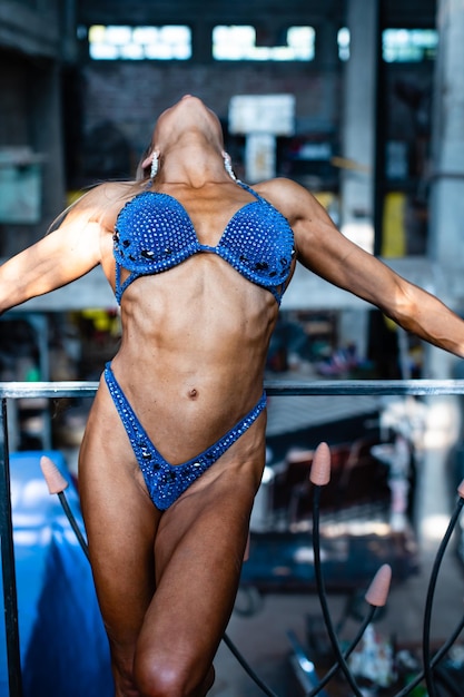 Foto campione di fitness femminile muscolare in bikini che posa in un ambiente industriale