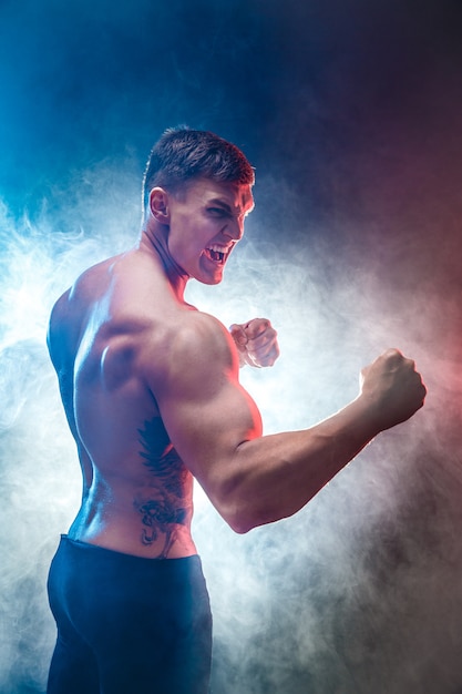 Muscular  fighter punching in smoke. Colour background.