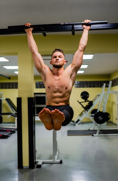 Muscular fit man doing pulling up on horizontal bar at gym