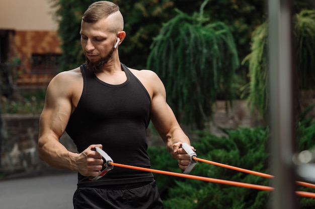 Muscular fitness coach doing exercises with stretching rubber outdoors