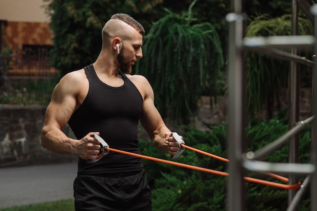 Muscular fitness coach doing exercises with stretching rubber\
outdoors