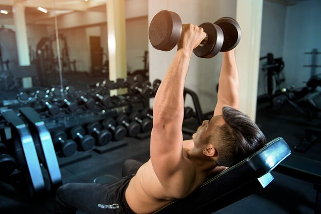 Muscular fitness man bodybuilder is workout with dumbbells in gym