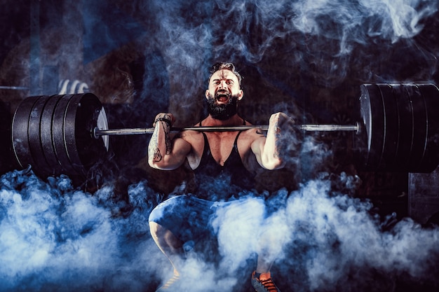 Muscular fitness man doing deadlift a barbell over his head in modern fitness center. Functional training.