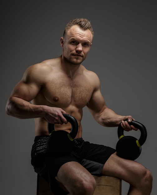 Muscular guy in black shorts sitting on podium and doing exercises with weights