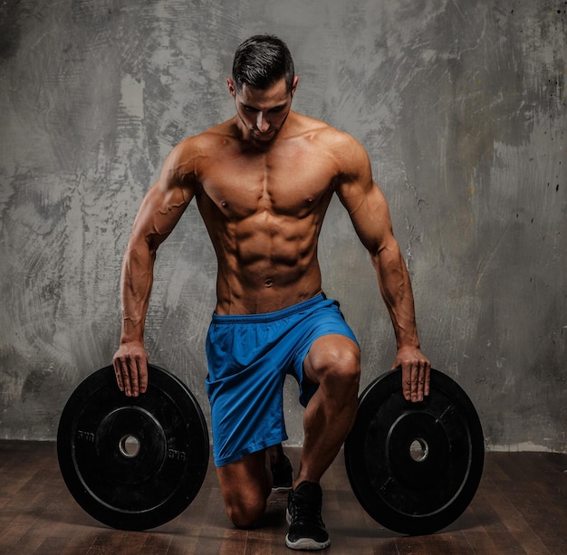 Muscular guy standing on knee and holding weights.