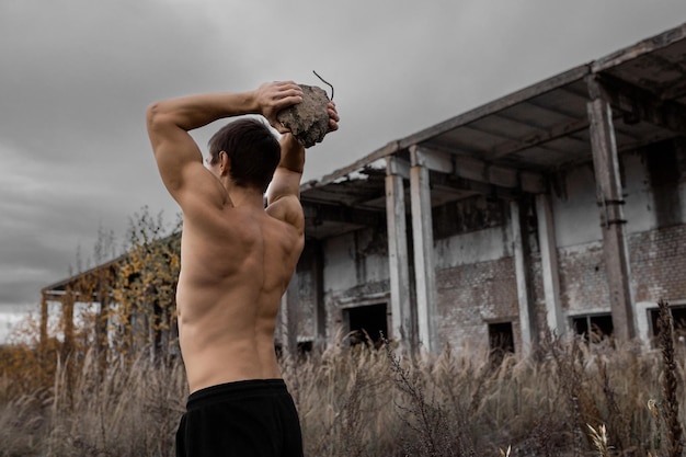 A muscular guy trains in the fresh air Workout and crossfit on the background of an old factory