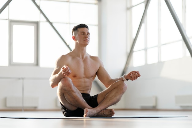 Muscoloso uomo ispanico con gli occhi chiusi seduto sul tappetino meditando concetto stile di vita sano