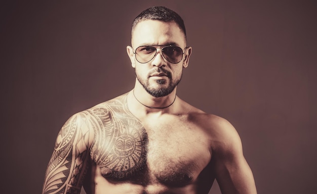 Muscular macho man with athletic body in sunglasses brutal sportsman torso steroids sport fitness health sexy abs of tattoo man male fashion confidence charisma