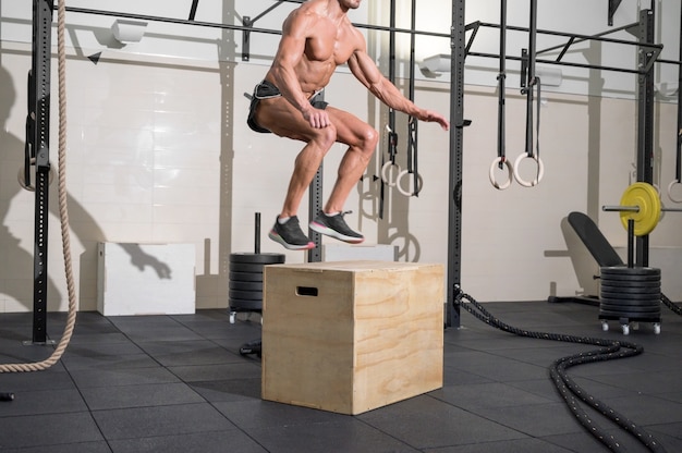 근육질의 남자 운동선수가 현대 헬스클럽 기능 훈련에서 나무 상자 위에서 점프하는 연습을 하고 있다