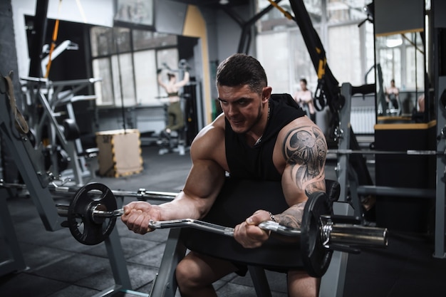 Atleta maschio muscolare che risolve con il bilanciere in palestra